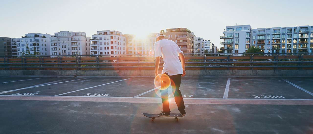 Photo of a skater with glaring sunset in the background in front of tower buildings who enjoys his hobby
